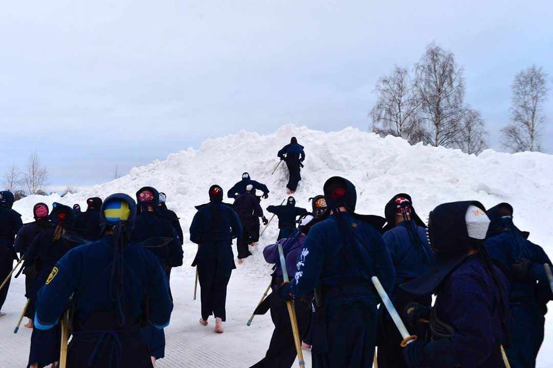 Kendoka in training kit run barefoot up a snow bank at a winter training camp